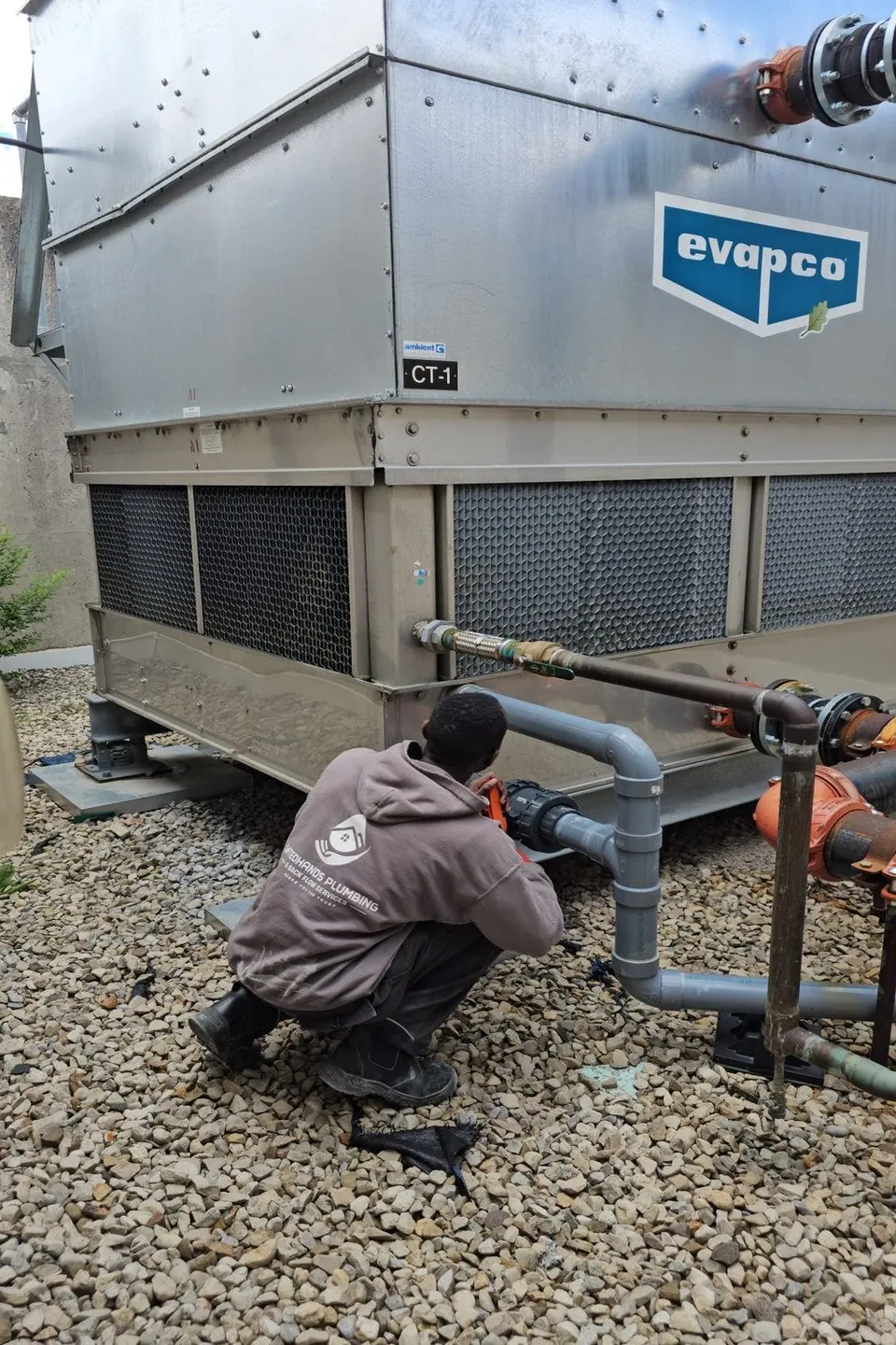 Plumbers connecting water lines to a rooftop cooling tower on a commercial building